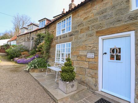 Exterior view of a stone cottage with a light blue door a white bench and plants at The Cottage in Sandsend