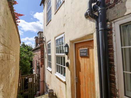 Narrow outdoor passage between buildings with door labeled Rooftops Cottage in Whitby