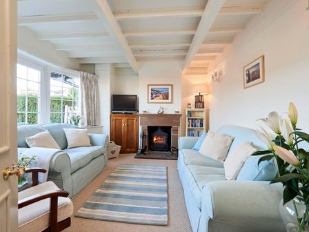 A living room with two blue sofas a striped rug a fireplace a wooden cabinet and windows with curtains at Rigg Cottage in Sandsend