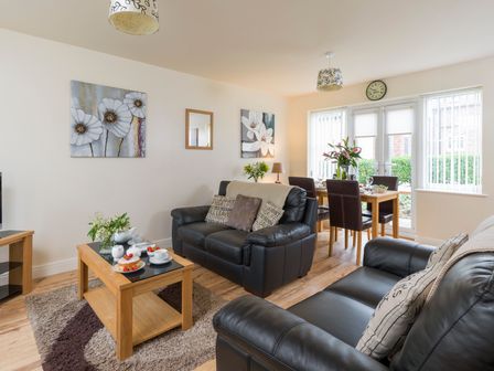 A living room with two black leather sofas a wooden coffee table and a dining table with chairs at Sunny Corner Cottage in Filey