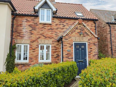 A brick house with a blue front door and windows surrounded by green hedges at Sleeper Cottage in Filey