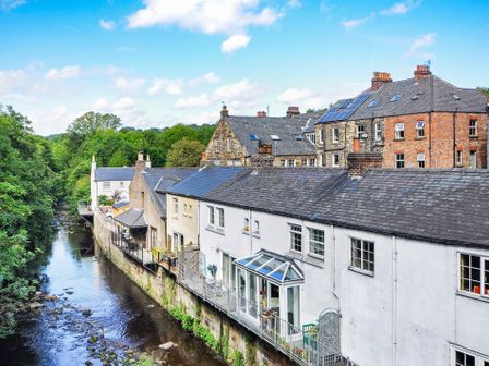 A row of houses along a river with trees in the background at Esk View Cottage in Grosmont