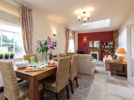 A dining area with a wooden table and wicker chairs next to a living room with sofas and a fireplace at Mews Cottage in Whitby
