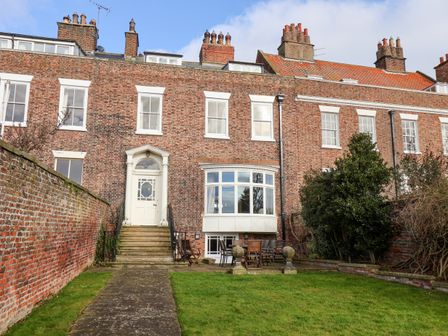 A brick terraced house with white framed windows a pathway leading to a door and a garden with outdoor furniture at 12 St Hildas in Whitby