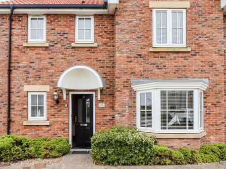 The front facade of a brick house with a black front door a white arched canopy and white-framed windows with greenery at Bay Cottage The Bay - Filey