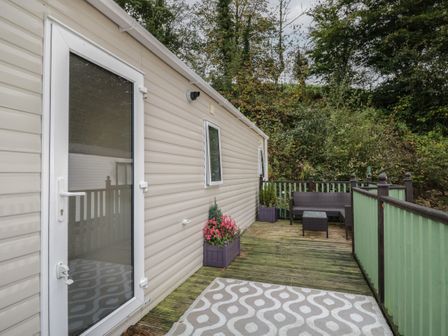 A deck area with a patterned rug outdoor seating and planters next to a beige mobile home at The Hideaway in Cockermouth