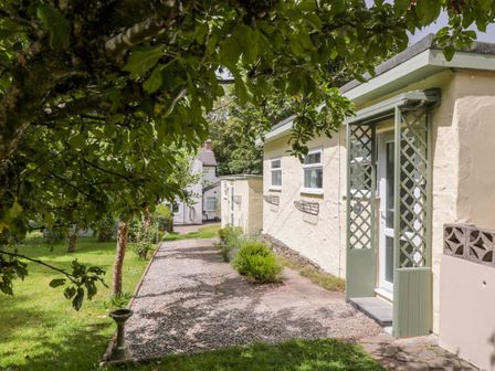 A garden path beside a cream building with windows and a green trellis door at The Roost in Camborne