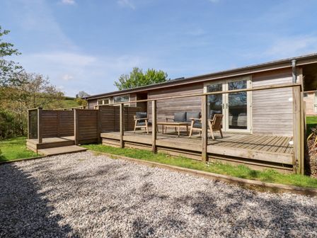 A wooden deck with outdoor seating and glass railing attached to a single-story building at 6 Valley View in Lanreath