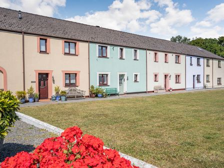 A row of terraced houses with front doors and windows with benches and potted plants on a grass lawn at Granary Cottage in Pembroke