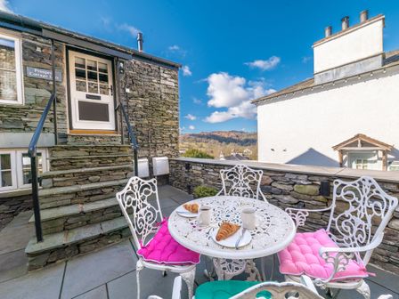 Outdoor patio with white metal table and chairs with colorful cushions and croissants at Prospect Cottage Loft in Ambleside