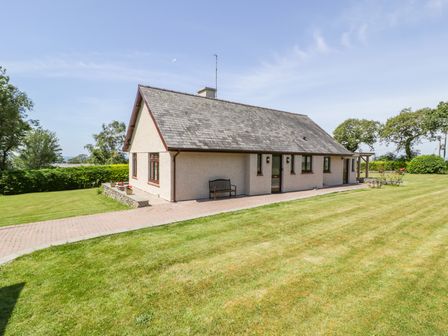 A single story house with a sloped roof surrounded by a lawn and a paved pathway at Berwyn in Talybont