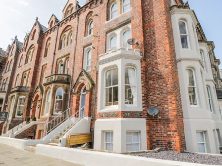 A row of red brick buildings with white trimmed windows and entrances on a sidewalk at 1 Church Square in Whitby