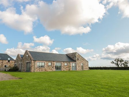 A stone house with multiple windows and a slate roof on a grassy lawn at The Long Barn in Berwick-Upon-Tweed