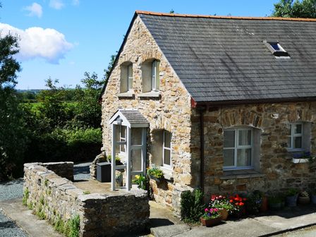 A stone cottage with a slate roof surrounded by plants and flowers outside at The Smithy in Dulas