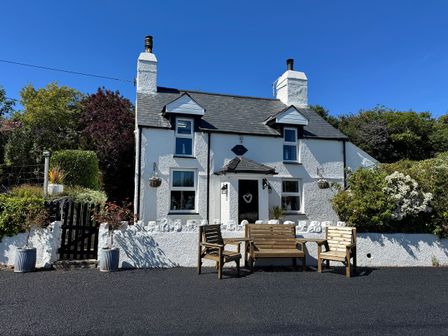A cottage with benches and a garden at Tan Yr Allt in Chwilog
