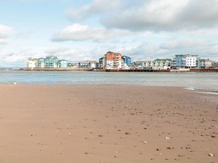 A waterfront scene with sandy beach and scattered stones leading to colorful buildings across the water at Sea Point in Exmouth