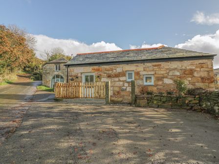 A stone building with small windows and a wooden fence in front on a paved area at The Bull Pen in Coombe near Grampound