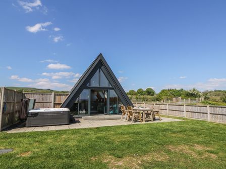 An outdoor patio with a hot tub and wooden table with chairs next to an a frame building at Elan Valley Welsh - The Sheepfold in Llanyre near Llandrindod Wells