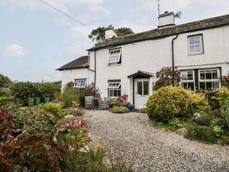 A white cottage with windows and a door surrounded by a gravel path and various bushes at Rusland View Rusland near Newby Bridge