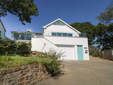 A modern white house with blue doors and windows with a driveway and glass balcony at Argraig in Llanbedrog