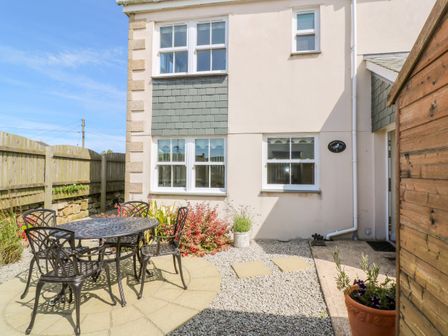 An outdoor patio area with a metal table and four chairs surrounded by gravel and plants at Henrys Croft in Lizard