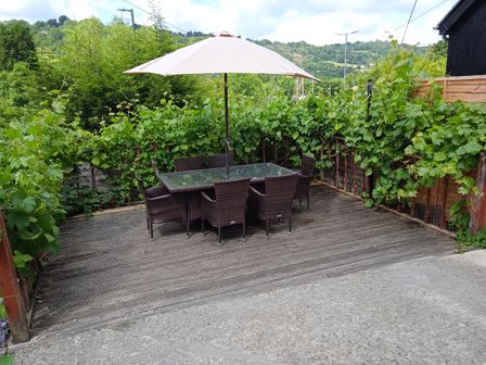 An outdoor patio with a glass table six chairs and a large umbrella surrounded by green plants