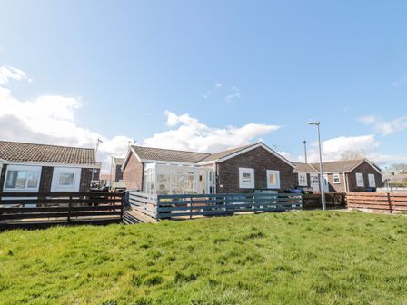 A row of single-story brick houses with fenced yards and a grassy area in front at The Snug in Beadnell