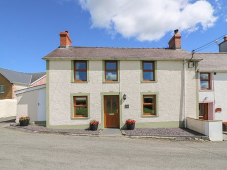 A two-story detached house with cream walls and brown window frames with flower pots outside at Gwynfa in Capel Iwan near Newcastle Emlyn