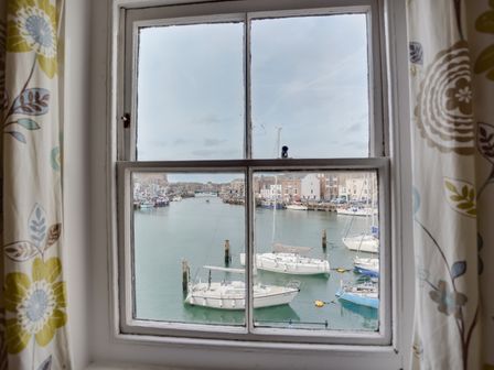 A window view of a harbor with sailboats and buildings in the background at The Ferryman in Weymouth