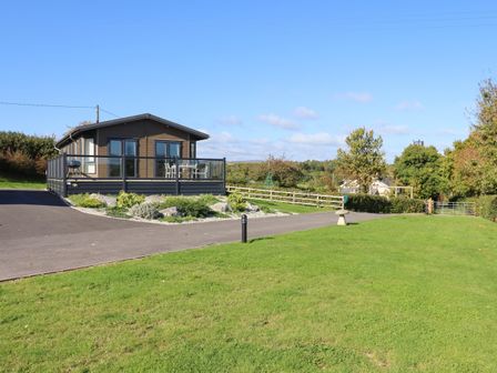 A detached cabin with a wraparound deck in a grassy rural setting at Alder Lodge in Teigngrace near Newton Abbot