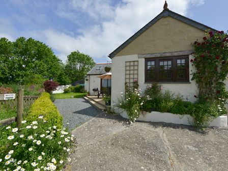 An outdoor view of a house with flower beds and a gravel driveway at Valley View in St Martin near Mawgan