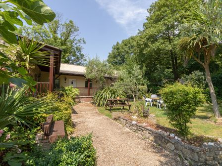 An outdoor garden area with a gravel path picnic table plastic chairs and trees at Riverhouse Lodge in Upwey