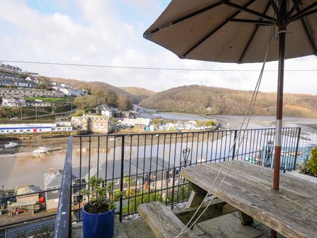 A balcony with a wooden picnic table and umbrella overlooking a river with boats and buildings at Elmbank in Looe