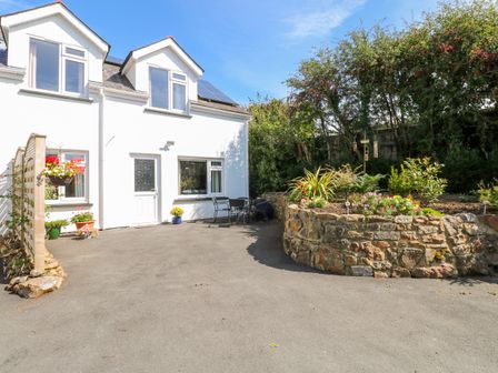 The exterior of a white two-story house with a paved driveway a circular raised stone flower bed and outdoor chairs at Little Freestone in Carew