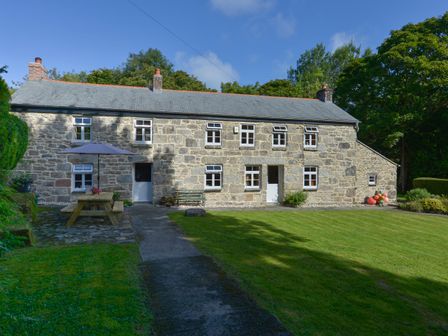 A stone cottage with white framed windows and doors a picnic table with an umbrella and green lawn at Heather Cottage in Nancledra