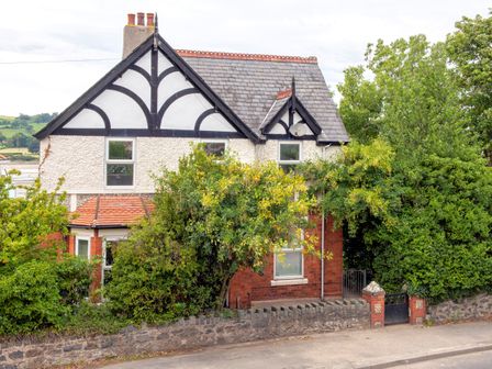 A two-story house with a tiled roof and black and white timber framing partially covered by trees and bushes at Bryn Y Mor in Conwy