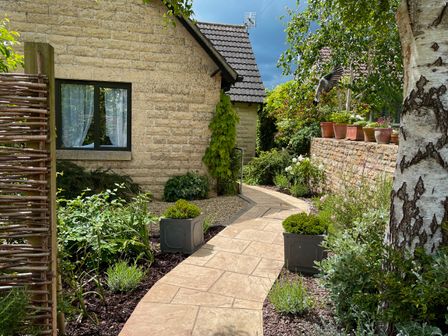 A garden pathway with plants and flowers beside a stone building at 1A Erneston Crescent in Corsham