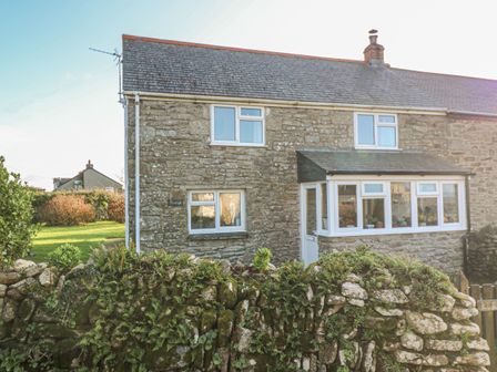 A stone cottage with white framed windows and a small garden behind a stone wall at Kernyk in Rinsey near Porthleven