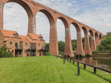 A brick viaduct over water next to brick houses with orange roofs and a green lawn at Maplebeck in Whitby