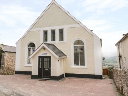 The exterior of a building with stained glass windows and a black door labeled saron at Saron Chapel in Penrhyn Bay