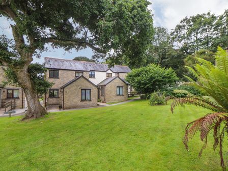 A stone house with a slate roof surrounded by grass trees and bushes at Deja Blue in Falmouth