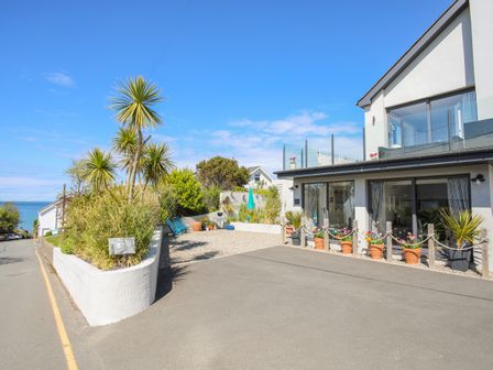 An outdoor area with potted plants and palm trees next to a modern building with glass windows at The Old Boat Store in Morfa Nefyn