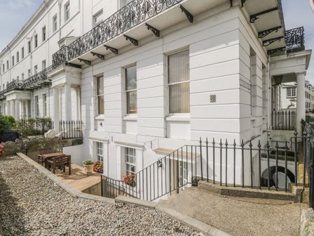 The exterior of a white terrace building with black iron railings and a small outdoor patio with a table and chairs at The Garden Apartment in Filey