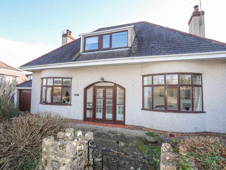 The front exterior of a two-story house with arched double doors and bay windows at Casita in Benllech