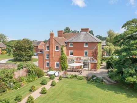 A large brick house with a garden patio and outdoor seating surrounded by greenery at Hilltop House in Tenbury Wells
