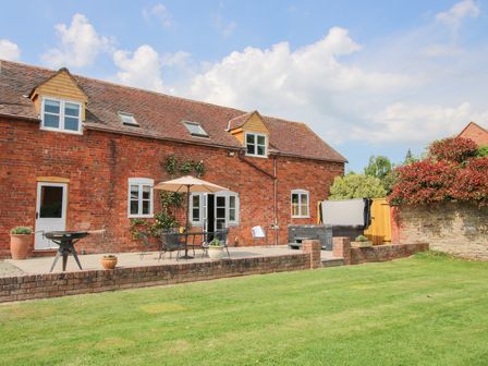A brick house with a patio table and umbrella in a garden at The Chestnuts in Tenbury Wells
