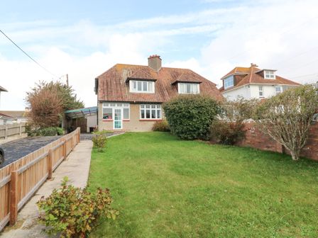 A semi detached house with a sloped roof and dormer windows with a driveway and green front lawn at Chilton in Bude