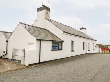 Exterior view of a white house with multiple windows and a gate at Tyddyn Serri in Rhosneigr