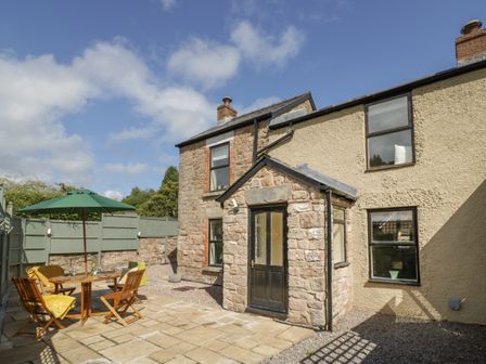 A stone and plaster exterior of a house with a patio set and green umbrella at Rainforest Cottage in Ruspidge