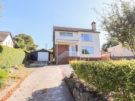 A two-story house with a driveway leading to a garage and bushes along the path at The Nook in Colwyn Bay